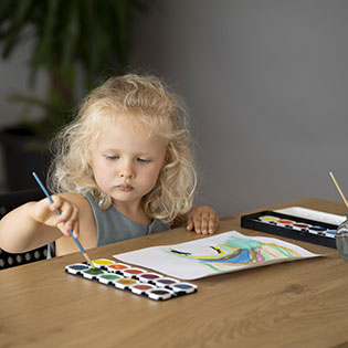 Young child painting with watercolors at a table.