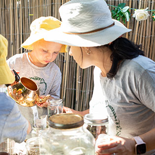 Woman and child pouring liquid into jars during an outdoor learning activity.